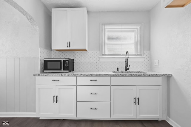 kitchen with dark hardwood / wood-style floors, sink, white cabinets, decorative backsplash, and light stone counters