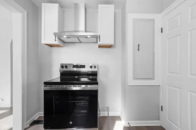 kitchen featuring dark wood-type flooring, white cabinets, stainless steel electric range oven, and wall chimney range hood