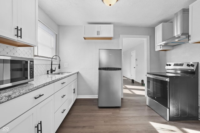 kitchen with appliances with stainless steel finishes, white cabinetry, sink, light stone countertops, and wall chimney exhaust hood