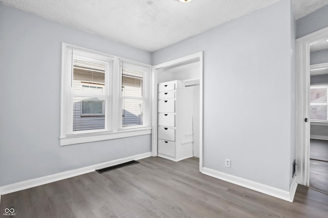 unfurnished bedroom featuring multiple windows, wood-type flooring, a textured ceiling, and a closet