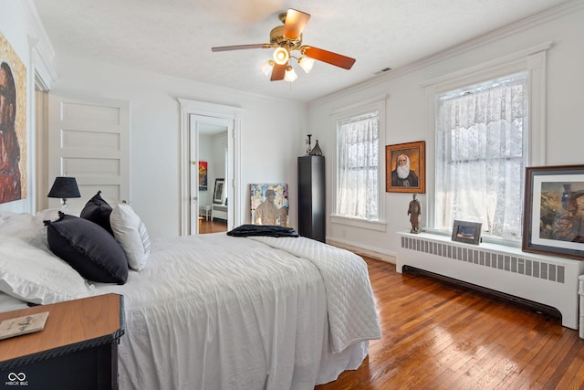 bedroom with radiator, hardwood / wood-style floors, ceiling fan, crown molding, and a textured ceiling