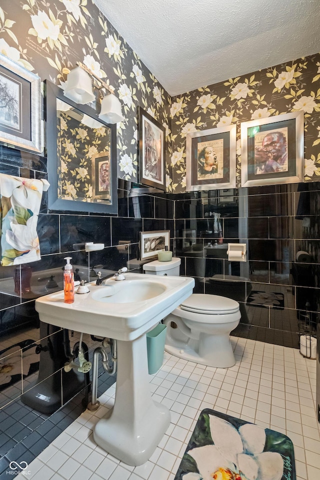 bathroom featuring tile patterned floors, toilet, a textured ceiling, and tile walls