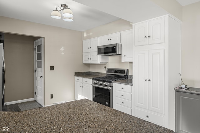 kitchen with appliances with stainless steel finishes, dark stone countertops, and white cabinets