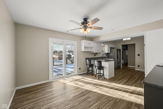 kitchen featuring dark wood-type flooring, a kitchen bar, sink, white cabinetry, and stainless steel fridge with ice dispenser