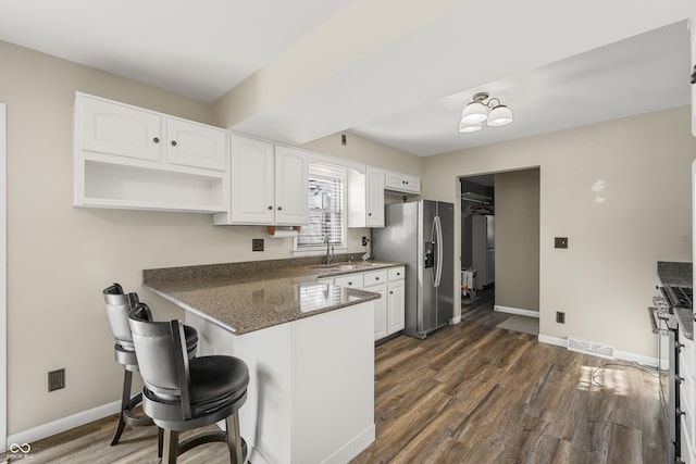 kitchen featuring sink, stainless steel refrigerator with ice dispenser, kitchen peninsula, white cabinets, and dark stone counters