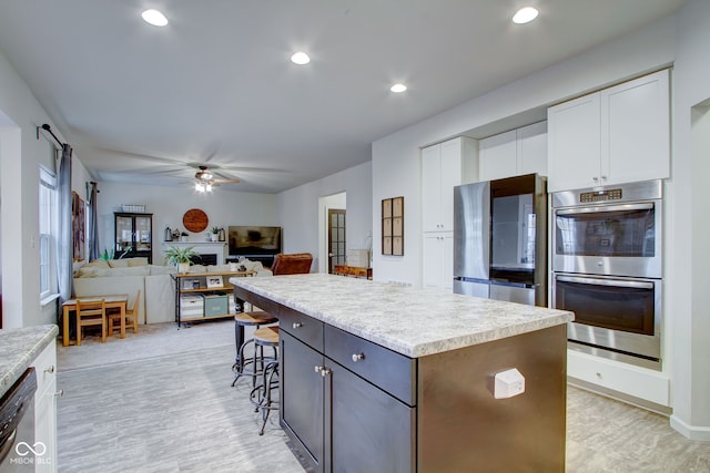 kitchen featuring a kitchen bar, a kitchen island, ceiling fan, stainless steel appliances, and white cabinets