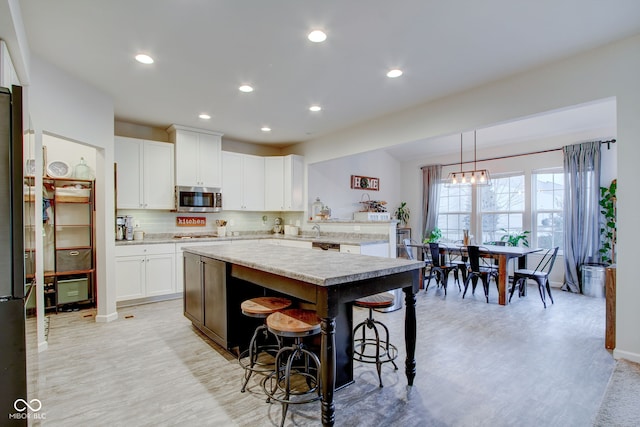 kitchen with a breakfast bar, appliances with stainless steel finishes, white cabinetry, hanging light fixtures, and a center island