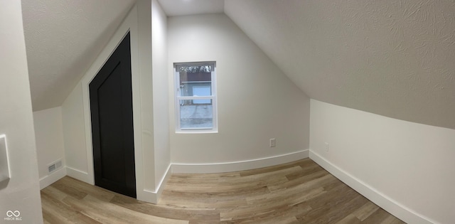 additional living space with lofted ceiling, a textured ceiling, and light wood-type flooring