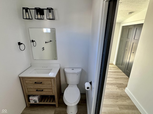 bathroom with vaulted ceiling, hardwood / wood-style floors, vanity, toilet, and a textured ceiling