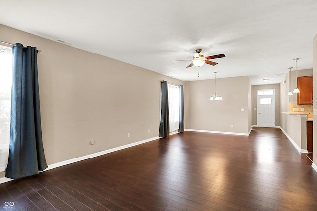 empty room with ceiling fan with notable chandelier, dark hardwood / wood-style floors, and a wealth of natural light