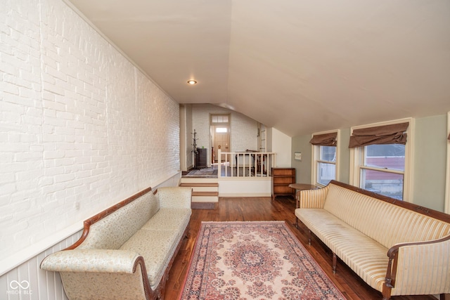 living room featuring vaulted ceiling, dark hardwood / wood-style floors, and brick wall