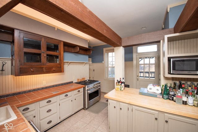 kitchen with sink, appliances with stainless steel finishes, tile counters, beamed ceiling, and white cabinets