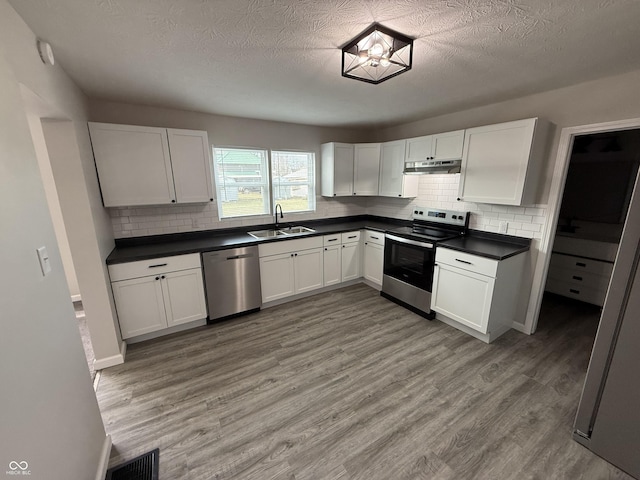 kitchen with appliances with stainless steel finishes, tasteful backsplash, wood-type flooring, sink, and white cabinets