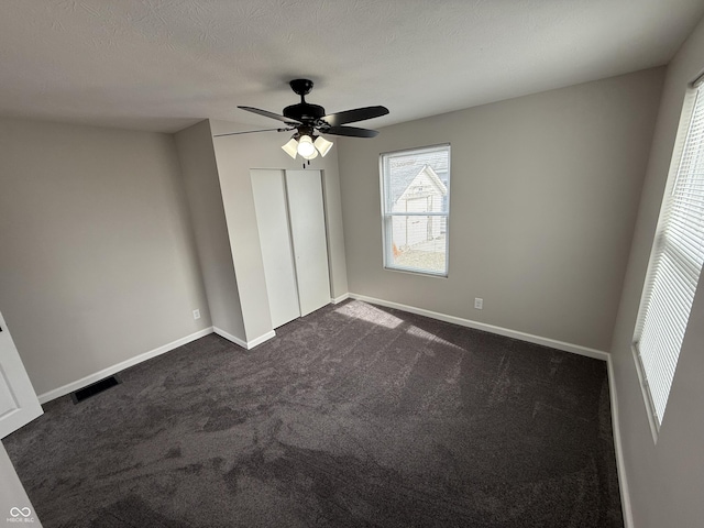 unfurnished bedroom with ceiling fan, dark carpet, a closet, and a textured ceiling