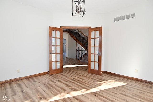 unfurnished room with an inviting chandelier, light wood-type flooring, and french doors