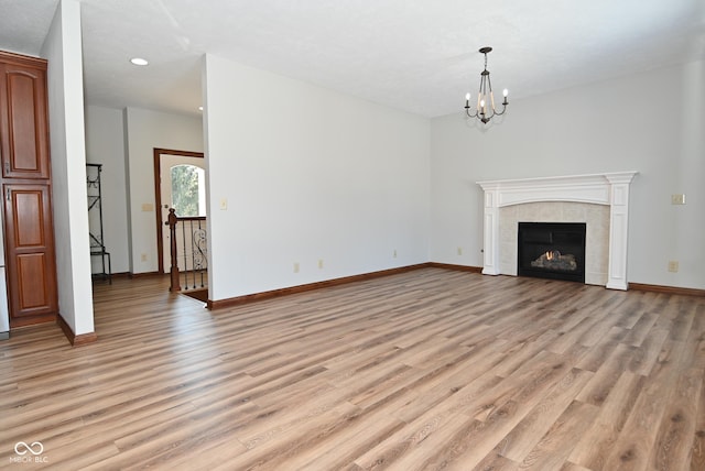 unfurnished living room with a chandelier, a tile fireplace, and light hardwood / wood-style flooring