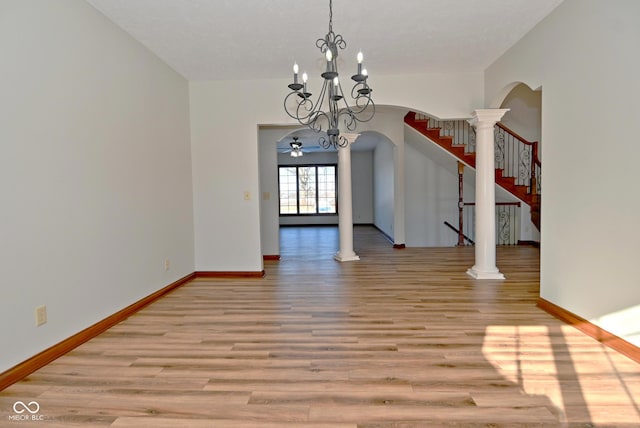 unfurnished dining area with ceiling fan with notable chandelier, light hardwood / wood-style flooring, and decorative columns