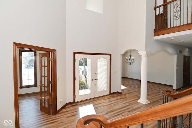 entrance foyer featuring decorative columns, a high ceiling, light hardwood / wood-style flooring, and french doors