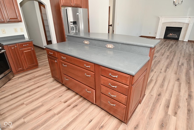 kitchen with stainless steel appliances, a tile fireplace, a kitchen island, and light hardwood / wood-style flooring