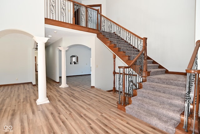 stairs with ornate columns, wood-type flooring, and a high ceiling