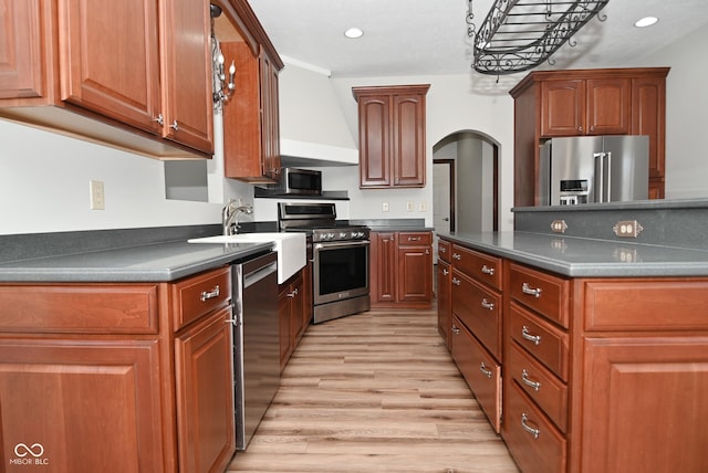 kitchen with stainless steel appliances, sink, wall chimney range hood, and light hardwood / wood-style floors