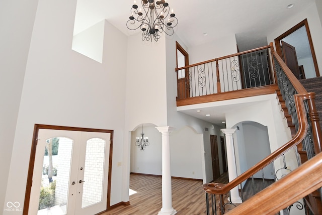 foyer entrance with light hardwood / wood-style flooring, decorative columns, a high ceiling, a notable chandelier, and french doors