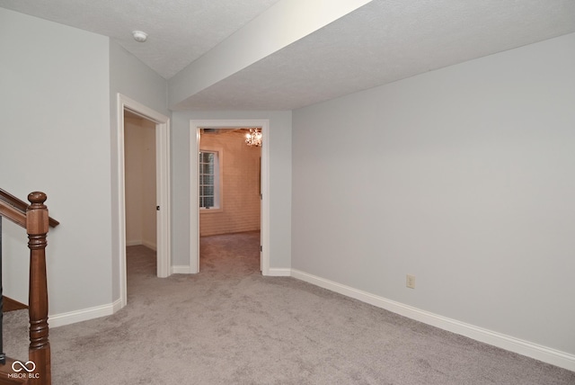 empty room with light colored carpet, a textured ceiling, and a notable chandelier