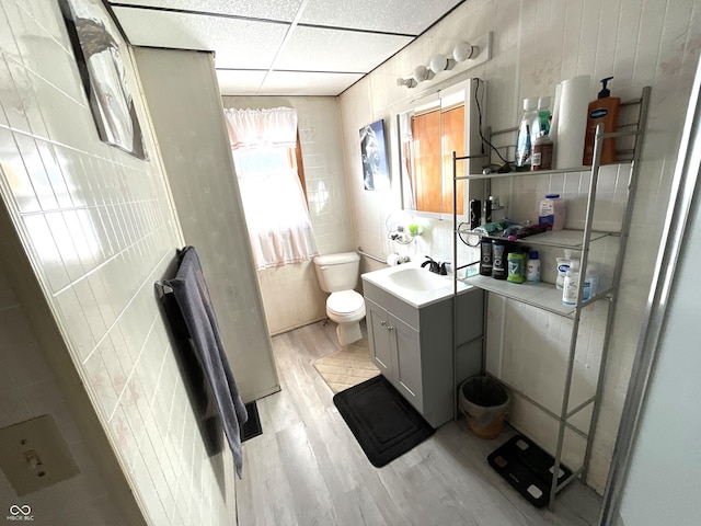 bathroom with tile walls, hardwood / wood-style floors, vanity, a drop ceiling, and toilet