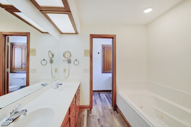 bathroom with a skylight, tiled bath, hardwood / wood-style flooring, vanity, and toilet