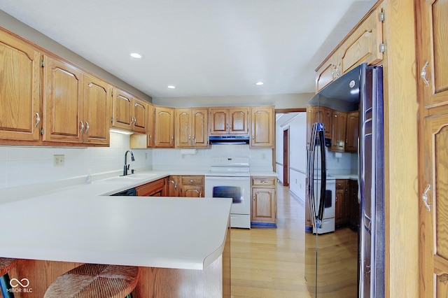 kitchen with a kitchen bar, sink, kitchen peninsula, electric stove, and backsplash