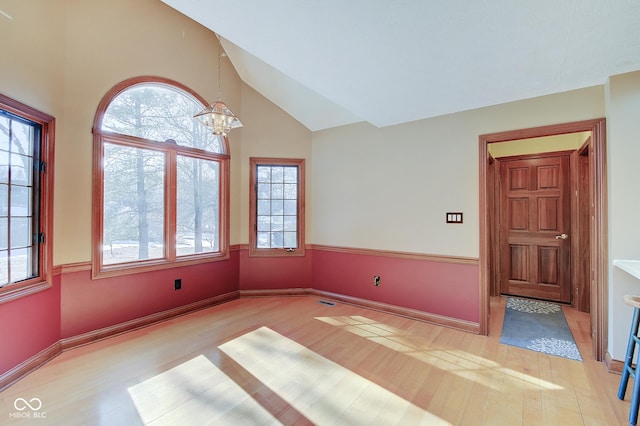 spare room with an inviting chandelier, high vaulted ceiling, and light wood-type flooring