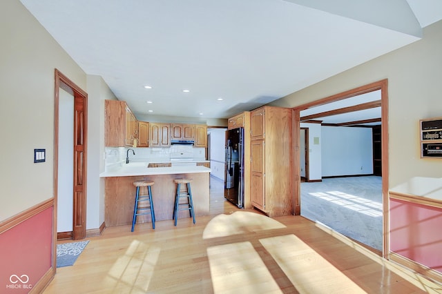 kitchen featuring a breakfast bar, black refrigerator, kitchen peninsula, stove, and backsplash