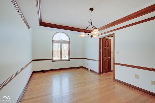 spare room featuring crown molding, a chandelier, light wood-type flooring, and a tray ceiling