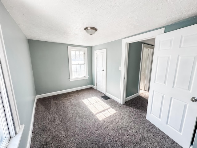 unfurnished bedroom featuring a textured ceiling, dark carpet, and a closet