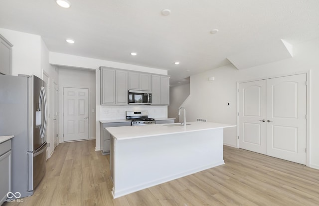 kitchen featuring gray cabinets, appliances with stainless steel finishes, sink, backsplash, and a kitchen island with sink