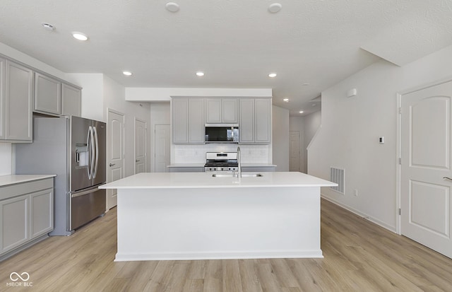 kitchen featuring a kitchen island with sink, backsplash, gray cabinets, and stainless steel appliances