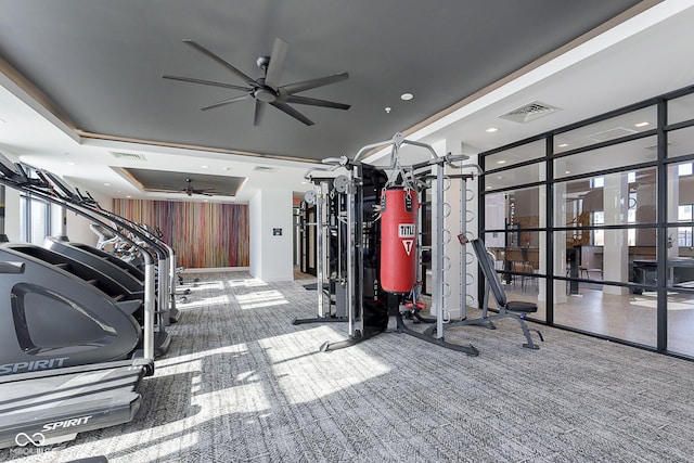 gym featuring carpet flooring, ceiling fan, and a tray ceiling