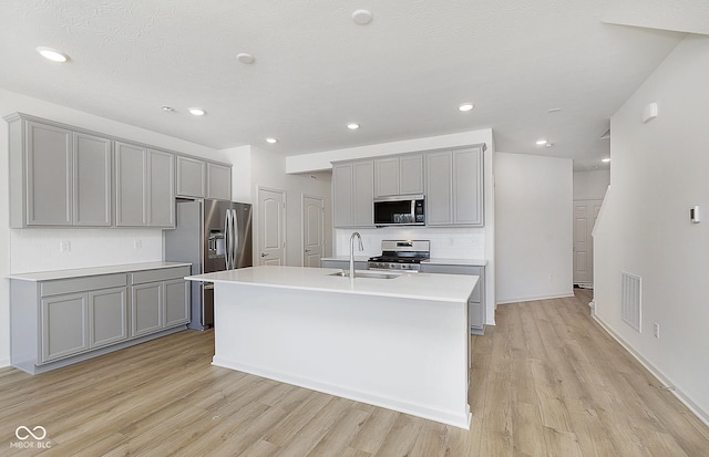 kitchen featuring sink, a center island with sink, appliances with stainless steel finishes, gray cabinets, and light hardwood / wood-style floors