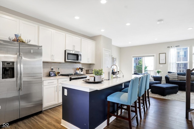 kitchen with white cabinetry, tasteful backsplash, dark hardwood / wood-style floors, stainless steel appliances, and a kitchen island with sink