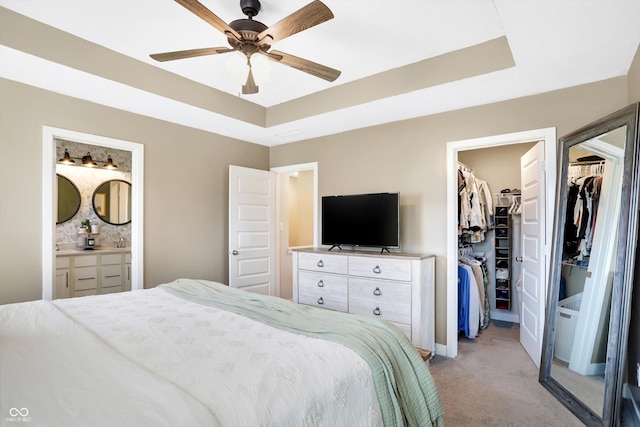 carpeted bedroom featuring connected bathroom, a tray ceiling, ceiling fan, and a spacious closet