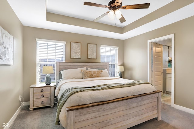 carpeted bedroom featuring a raised ceiling, ceiling fan, and ensuite bathroom