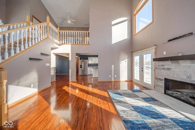 living room featuring french doors, a stone fireplace, hardwood / wood-style floors, and a high ceiling