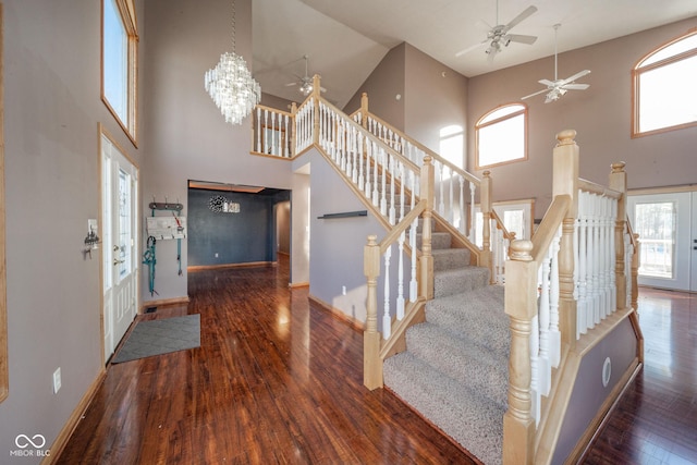 foyer entrance with ceiling fan with notable chandelier, a towering ceiling, and dark wood-type flooring