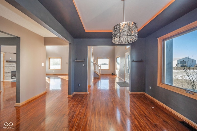 unfurnished dining area with a tiled fireplace, wood-type flooring, a chandelier, and a tray ceiling