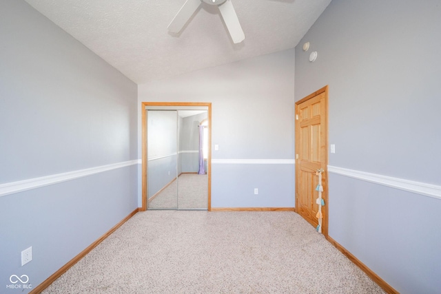 unfurnished bedroom with vaulted ceiling, light colored carpet, a textured ceiling, a closet, and ceiling fan