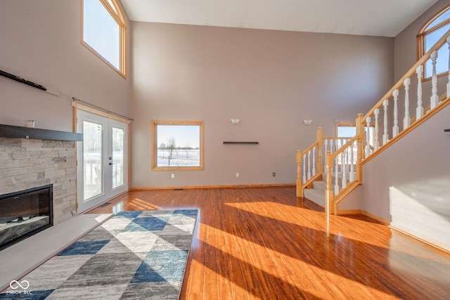 living room featuring hardwood / wood-style flooring, a stone fireplace, a towering ceiling, and french doors