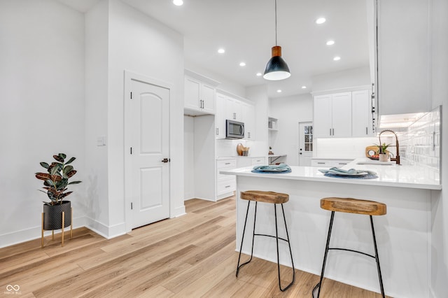 kitchen with decorative light fixtures, white cabinetry, sink, and kitchen peninsula