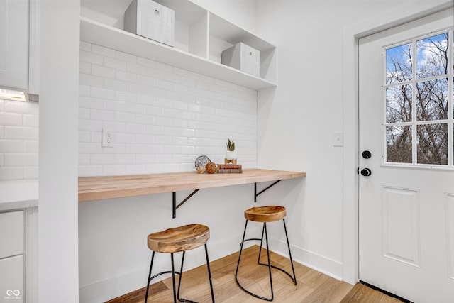 kitchen with butcher block countertops, a breakfast bar, light hardwood / wood-style floors, and backsplash