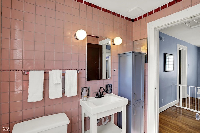 half bathroom with baseboards, tile walls, toilet, and wood finished floors