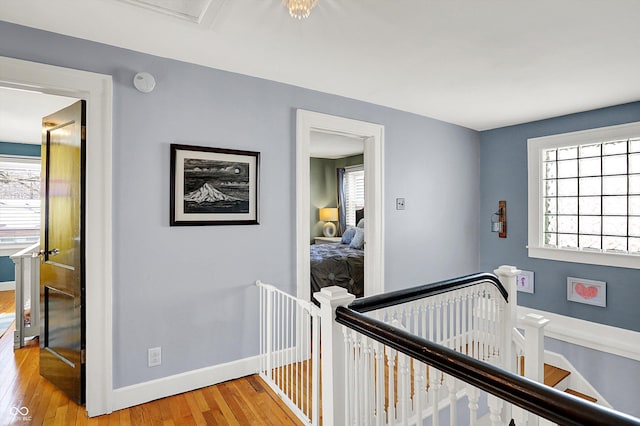 corridor with a wealth of natural light, baseboards, light wood finished floors, and an upstairs landing